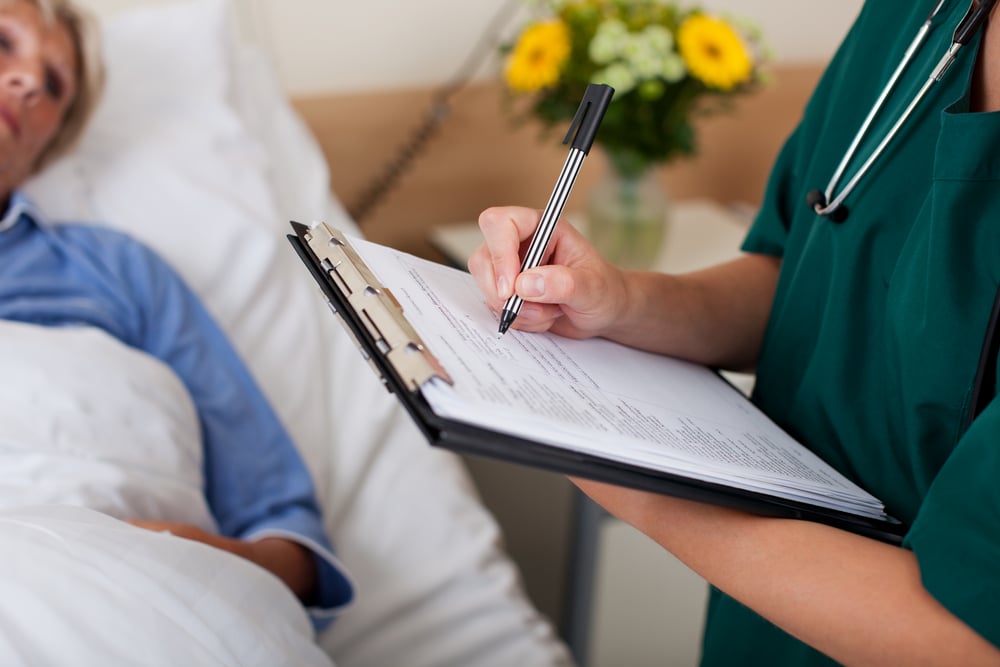 Writing on clipboard with patient in background in hospital Writing on clipboard with patient in background in hospital